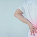 a person holding their lower back in pain, highlighting discomfort in the lumbar region and surrounding area.