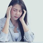 a woman holding her head in distress while working at a laptop, possibly depicting symptoms of stress-related pain