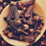 whole cloves and dried clove buds in a wooden spoon on a bed of cloves, highlighting natural spice remedies