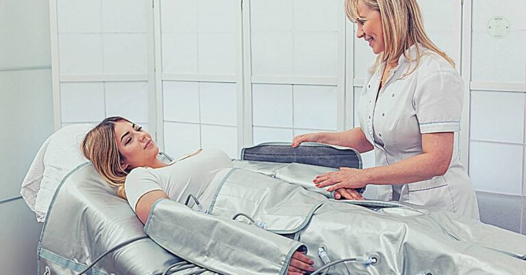 a woman receiving manual lymphatic drainage treatment while lying on a specialized massage table with a therapist assisting