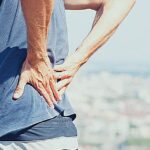 Jak Si Rychle Ulevit Od Bolesti Bederní Páteře! 7 a person holding lower back in pain, demonstrating common symptoms of bolest bederní páteře outdoors.