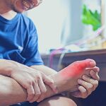 a person gently holding and massaging an elderly person’s swollen big toe joint, likely addressing hallux valgus or joint pain relief.