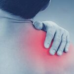 a person holding their right shoulder area highlighting pain in the rameno kloub region, indicating possible poškodění or discomfort.
