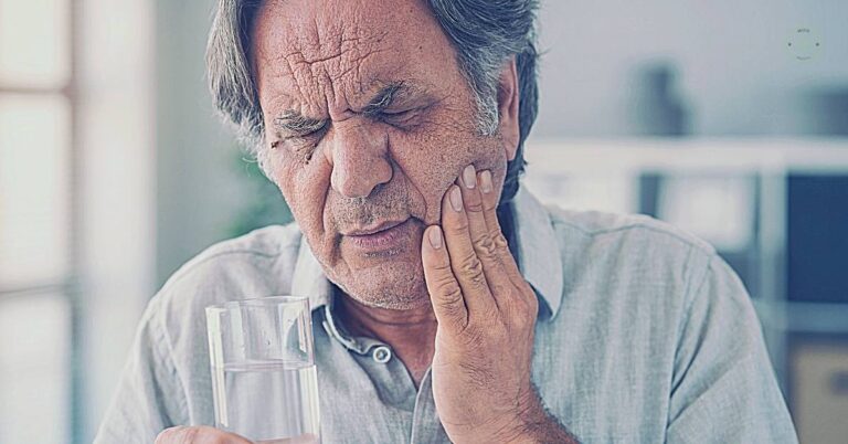 an elderly person holding a glass of water while holding their jaw, appearing to experience toothache pain