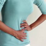 a person holding their lower left abdomen area indicating possible discomfort or pain.