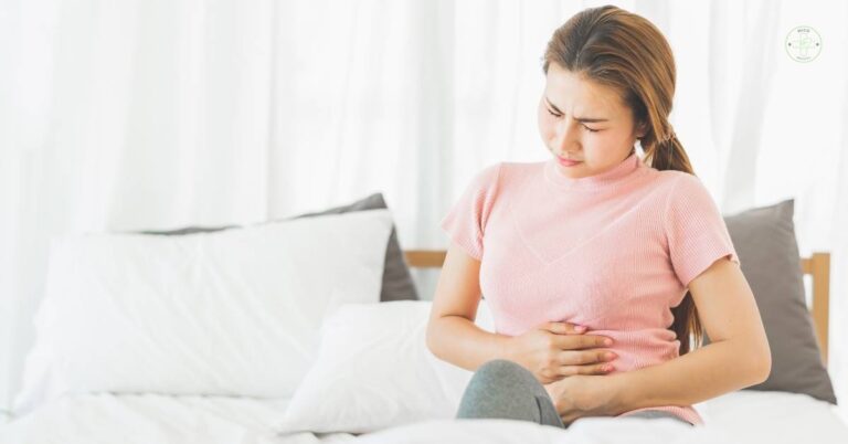 a woman experiencing abdominal pain while sitting on a bed, clutching her stomach.