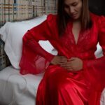 a person in red robe sitting on bed holding abdomen area, possibly indicating discomfort or pain.