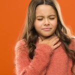 a young person holding their throat while showing signs of discomfort, possibly indicating bolest v krku