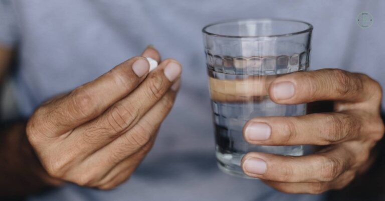 a person holding a small white pain relief tablet and a glass of water, ready to take a volně prodejné léky proti bolesti.