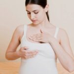a woman examining her breast, illustrating potential breast tenderness or sensitivity during early pregnancy