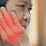 a person holding their jaw in pain, highlighting affected area with red glow, illustrating příznaky bolesti čelisti