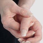6 Hlavních Přičin Bolesti Palce u Ruky & Jejich Léčba! 5 a person holding a thumb affected by joint discomfort, possibly indicating symptoms of hand or thumb pain.