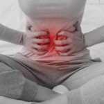 a person clutching their lower abdomen highlighting ovulační bolest during mittelschmerz with a glowing red area.
