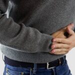 a person clutching their lower abdomen, indicating possible abdominal pain or discomfort in the pelvic region.