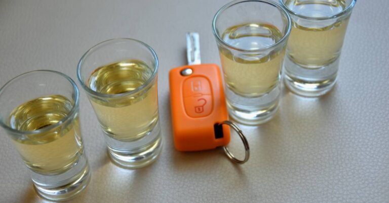 four glasses filled with alcoholic beverages and an orange car key fob on a keyring, illustrating the risk of drinking and driving