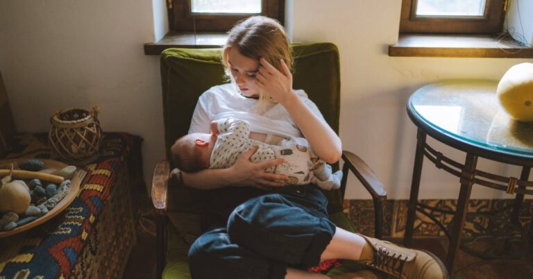 a young mother sitting and holding a baby with a concerned expression, possibly experiencing discomfort or pain while breastfeeding