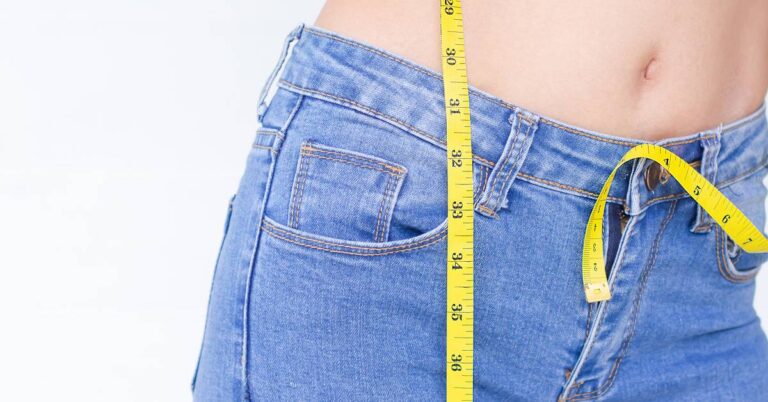 Kalkulačka WHR Indexu: Co Nám Prozradí Poměr Boků A Pasu O Našem zdraví? 4 a person measuring their waist with a tape measure against blue jeans to assess body proportions and health metrics