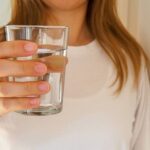 a person holding a clear glass of water, illustrating proper hydration for maintaining health and energy