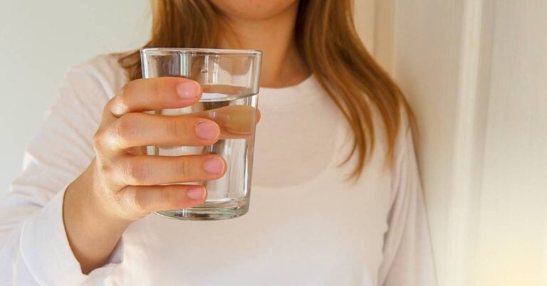 Kalkulačka Pitného Režimu: Zjistěte Kolik Vody Máte Pít! 8 a person holding a clear glass of water, illustrating proper hydration for maintaining health and energy