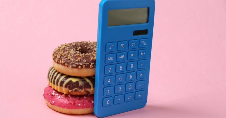 a blue calculator leaning against a stack of three decorated doughnuts, illustrating energy value comparison in nutrition.