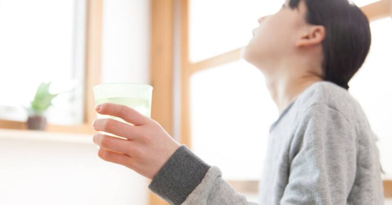 a person holding a small glass of green herbal tea or gargle mixture, likely for natural throat relief.