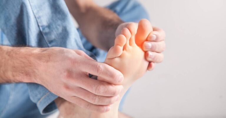 a person holding and examining a swollen, red toe on their foot, indicating possible zánět or bolest prstů na noze.