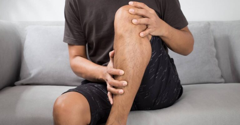 a person holding and examining their knee joint, indicating possible bolest dolních končetin around the koleno