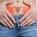a person holding their lower abdomen with an overlay of highlighted female reproductive organs showing an ovarian cyst rupture, emphasizing acute pelvic pain.