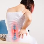 a person experiencing lower back pain near the sacrum while demonstrating manual mobilization of the sacroiliac region.