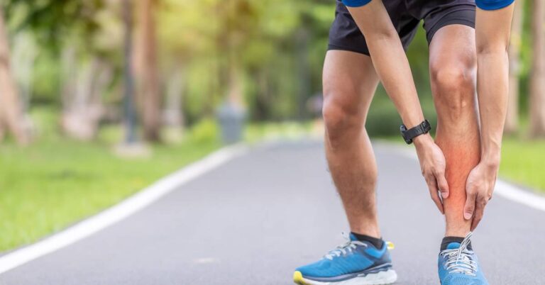 a person holding their calf while standing on a paved path, showing signs of discomfort or pressure in the lower leg.