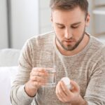 a man taking a pill from a bottle with a glass of water, considering health and medication.