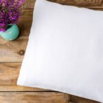 a white orthopedic cervical pillow placed on a wooden surface beside a small vase with purple flowers