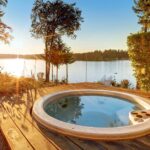 a serene outdoor wooden deck with an inflatable hot tub surrounded by lush greenery and a scenic lake at sunset