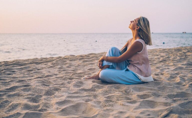 a woman practicing deep breathing and relaxation by the seaside, embodying calm for postizometrická relaxace techniques.