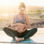 Wellness v těhotenství: Jak správně pečovat o své tělo během těhotenství 11 a pregnant woman practicing relaxed yoga or meditation outdoors on a wooden deck, holding her belly with a serene smile.