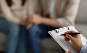 a professional counselor taking notes during a consultation with a couple in distress, holding a clipboard with a pen