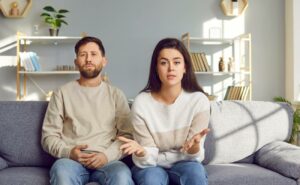 a couple sitting on a couch in a cozy living room, gesturing as if discussing a topic related to zlepšení komunikace during what appears to be a serious conversation.
