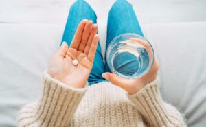 a person holding a pill in one hand and a glass of water in the other, ready to take medication for pain or inflammation relief