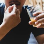 a person taking a pill while holding a glass of alcoholic beverage, illustrating potential medication and alcohol combination