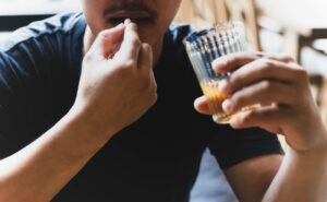 a person taking a pill while holding a glass of alcoholic beverage, illustrating potential medication and alcohol combination