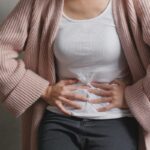 Bolest břicha uprostřed pod žebry: 6 Nejběžnějších příčin 9 a person holding their mid-abdomen under ribs, indicating gastrointestinal discomfort or abdominal pain.