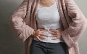 a person holding their mid-abdomen under ribs, indicating gastrointestinal discomfort or abdominal pain.
