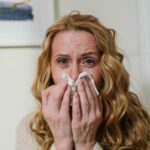a person covering their face with tissues, showing signs of distress possibly due to allergies affecting well-being