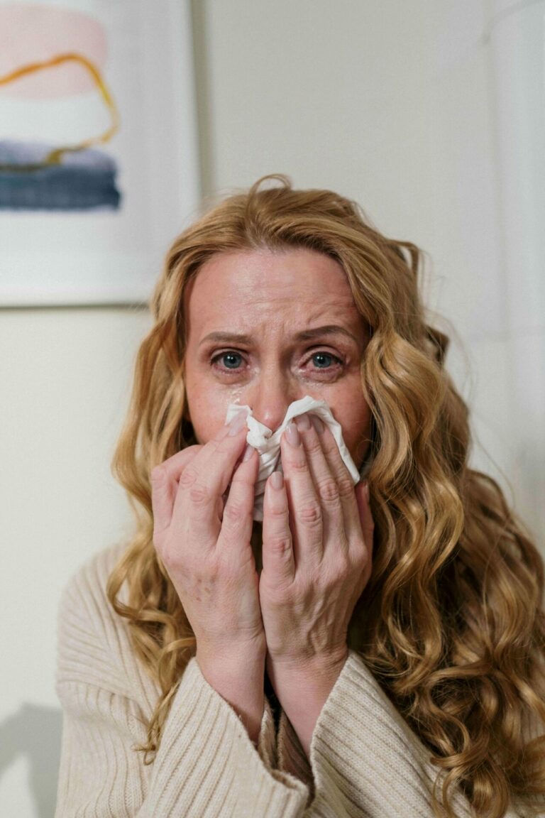 a person covering their face with tissues, showing signs of distress possibly due to allergies affecting well-being