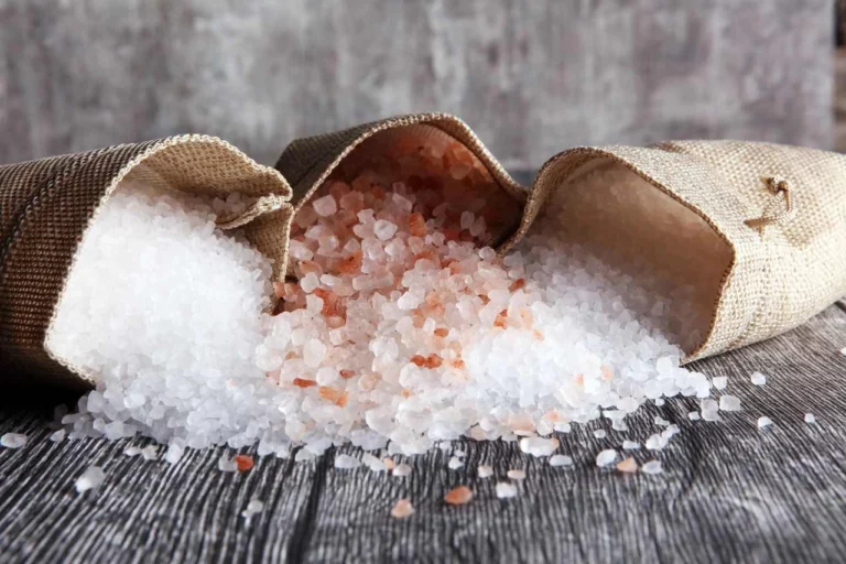 a burlap sack spilling coarse, natural Himalayan pink salt crystals onto a textured surface